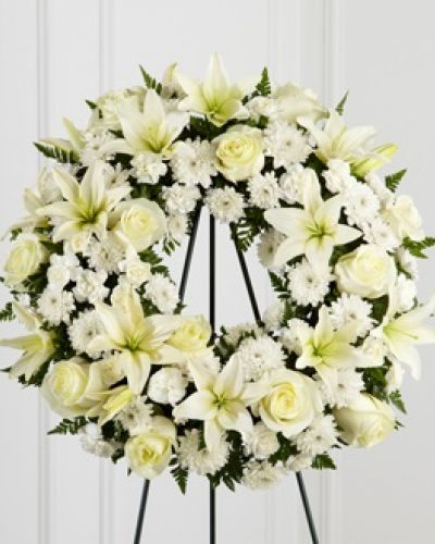 The FTD® Treasured Tribute™ Wreath offers peaceful wishes of heartfelt sympathy with each delicate bloom. Bright white roses, Asiatic lilies, mini carnations and cushion poms are beautifully arranged to form an elegant accented with lush and vibrant greens. Displayed on a wire easel, this gorgeous tribute is a wonderful symbol of eternal life and sweet serenity.